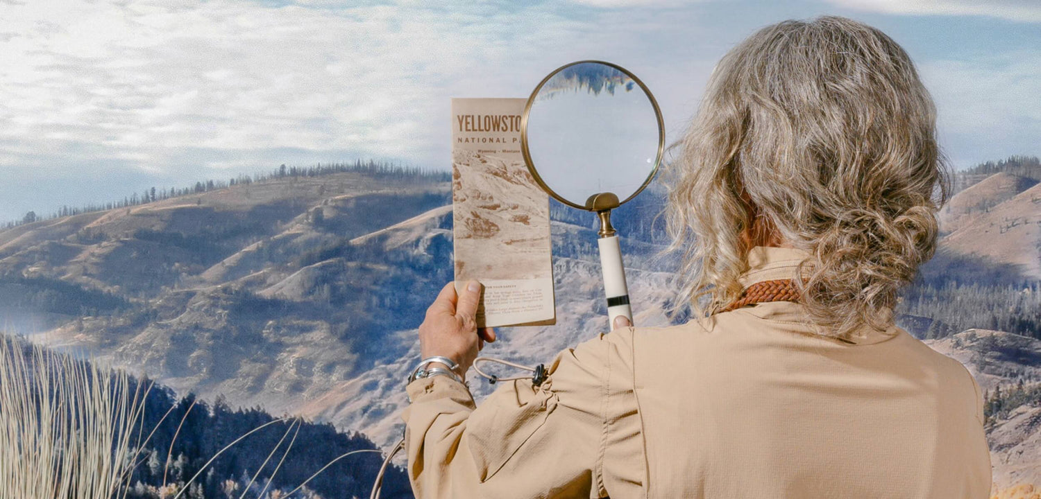 Woman wearing the Tackle Suit with a magnifying glass looking at a map at Yellowstone